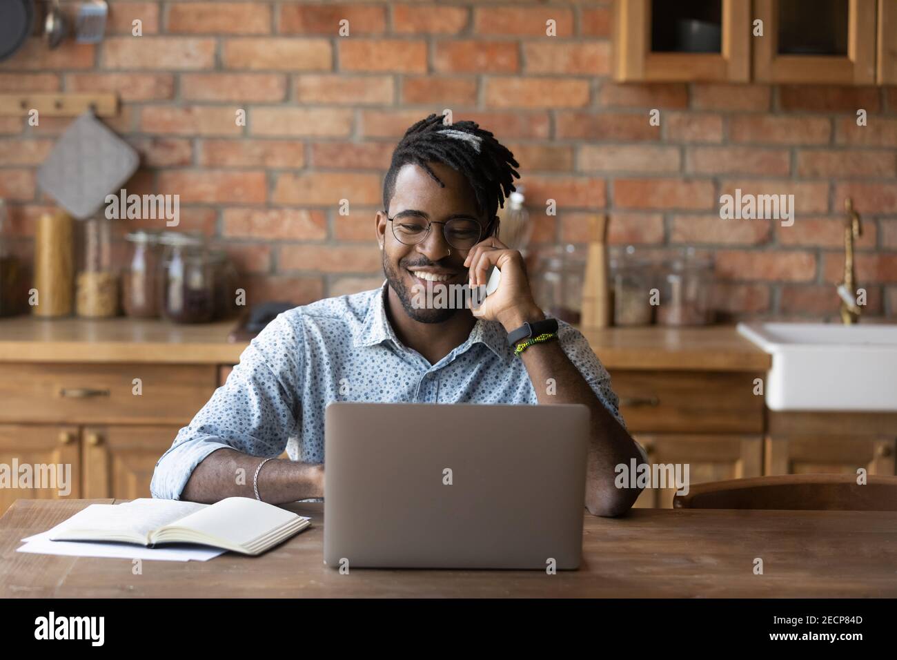 Smiling African American man talking on phone, using laptop Stock Photo