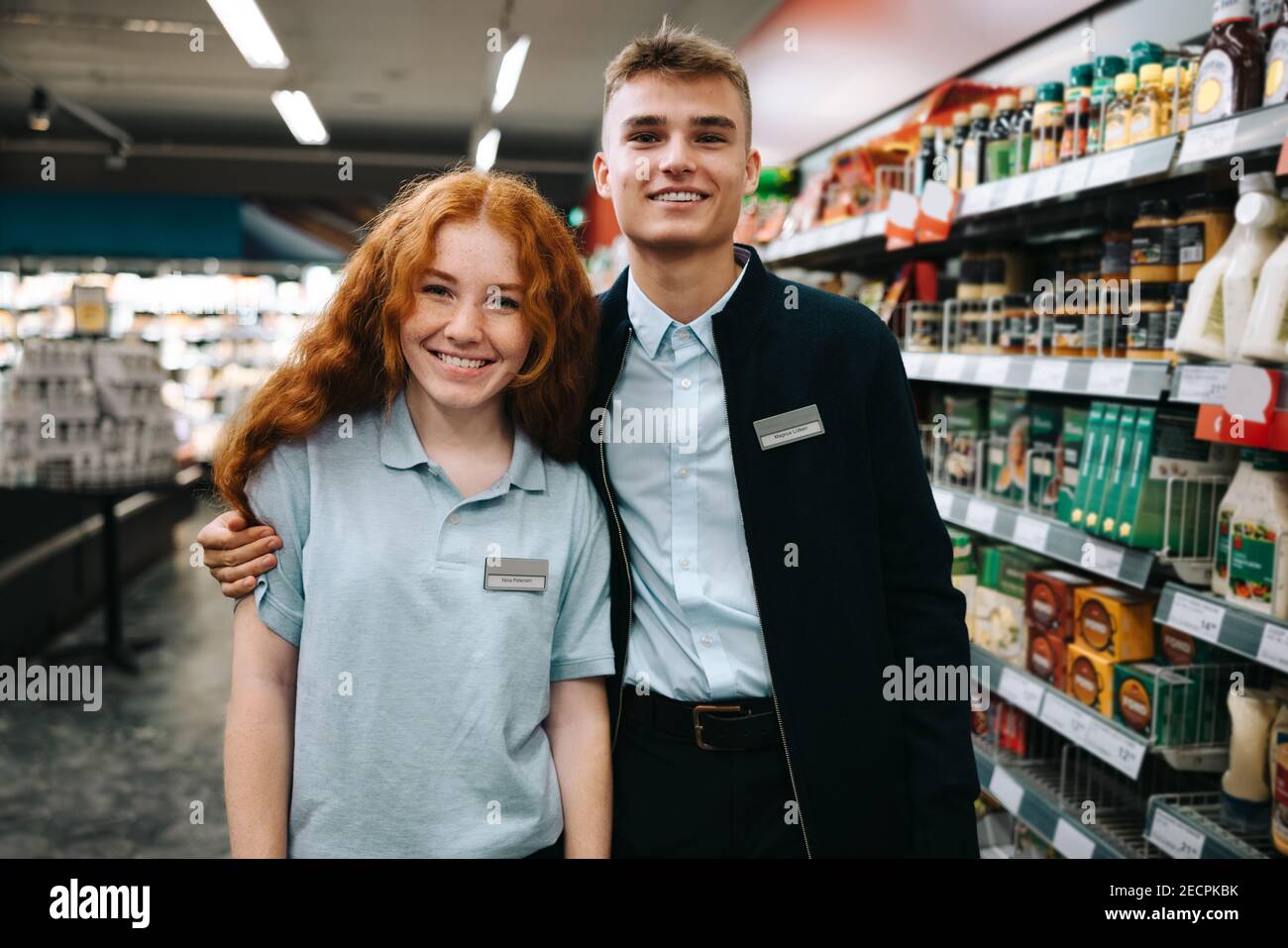 Trainee employees of supermarket. Man and woman standing together and looking at camera in grocery store. Stock Photo