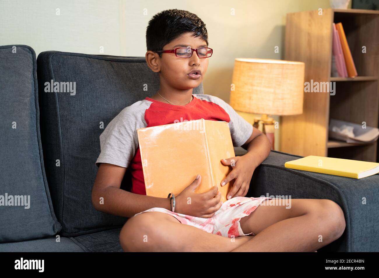 young kid mugging up answers from book during exams with out understanding the concepts at home on sofa - concept of education system and teenager Stock Photo