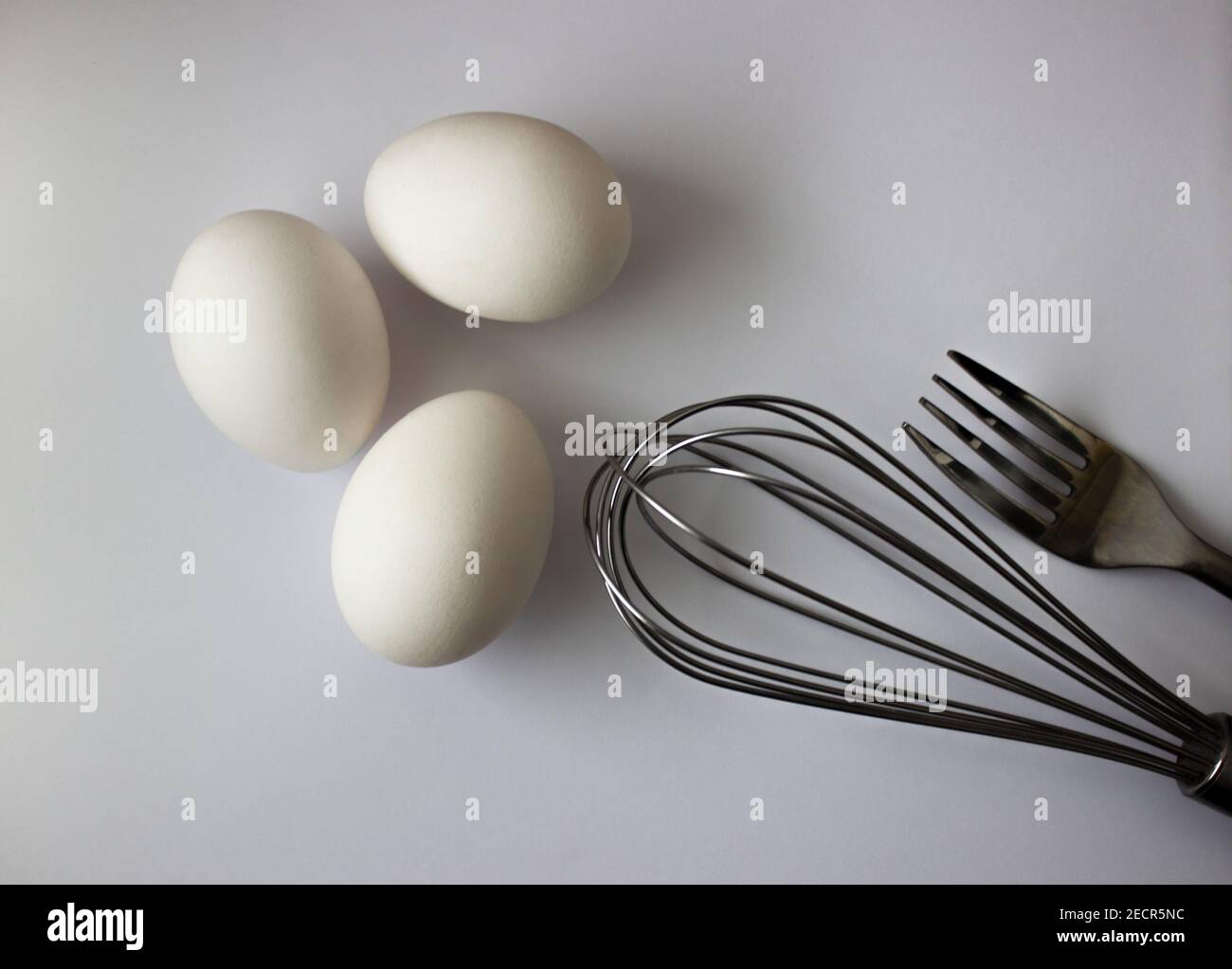 three chicken white eggs whisk and fork on gray background Stock Photo