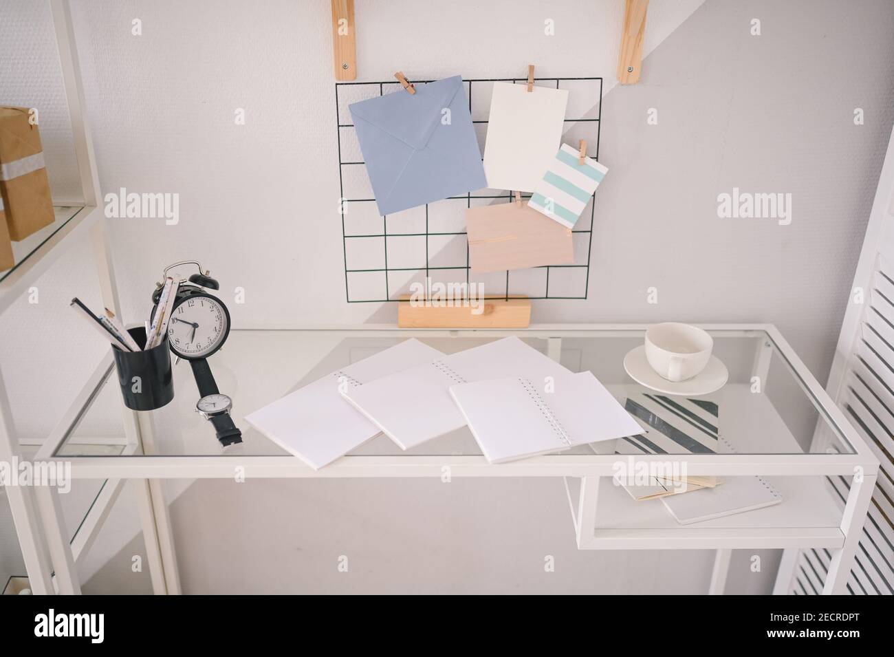 Background image of empty home cozy office working space modern scandinavian design. White glass table, holder lattice for notes with stylish decor elements, stationery, alarm clock and wristwatch Stock Photo