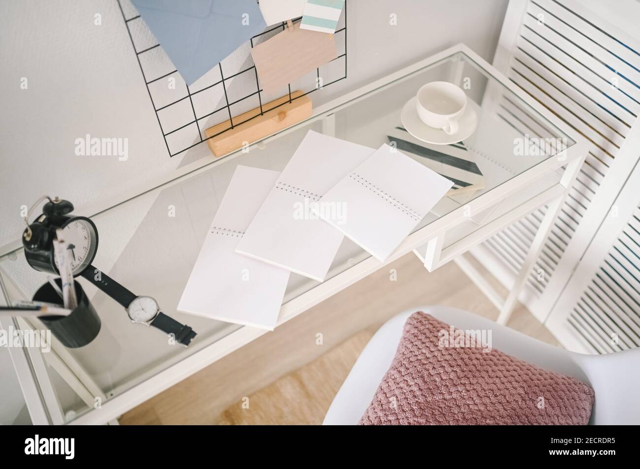 Background image of empty home cozy office working space modern scandinavian design. White glass table, holder lattice for notes with stylish decor elements, stationery, alarm clock and wristwatch Stock Photo