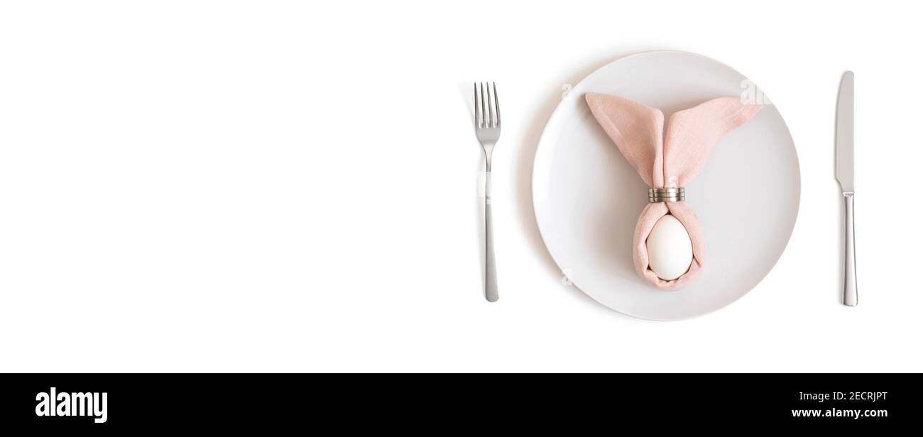 Beautiful Easter table setting with a white egg on a pink napkin with rabbit ears on a white background. Banner. Easter concept. Space for text. Stock Photo