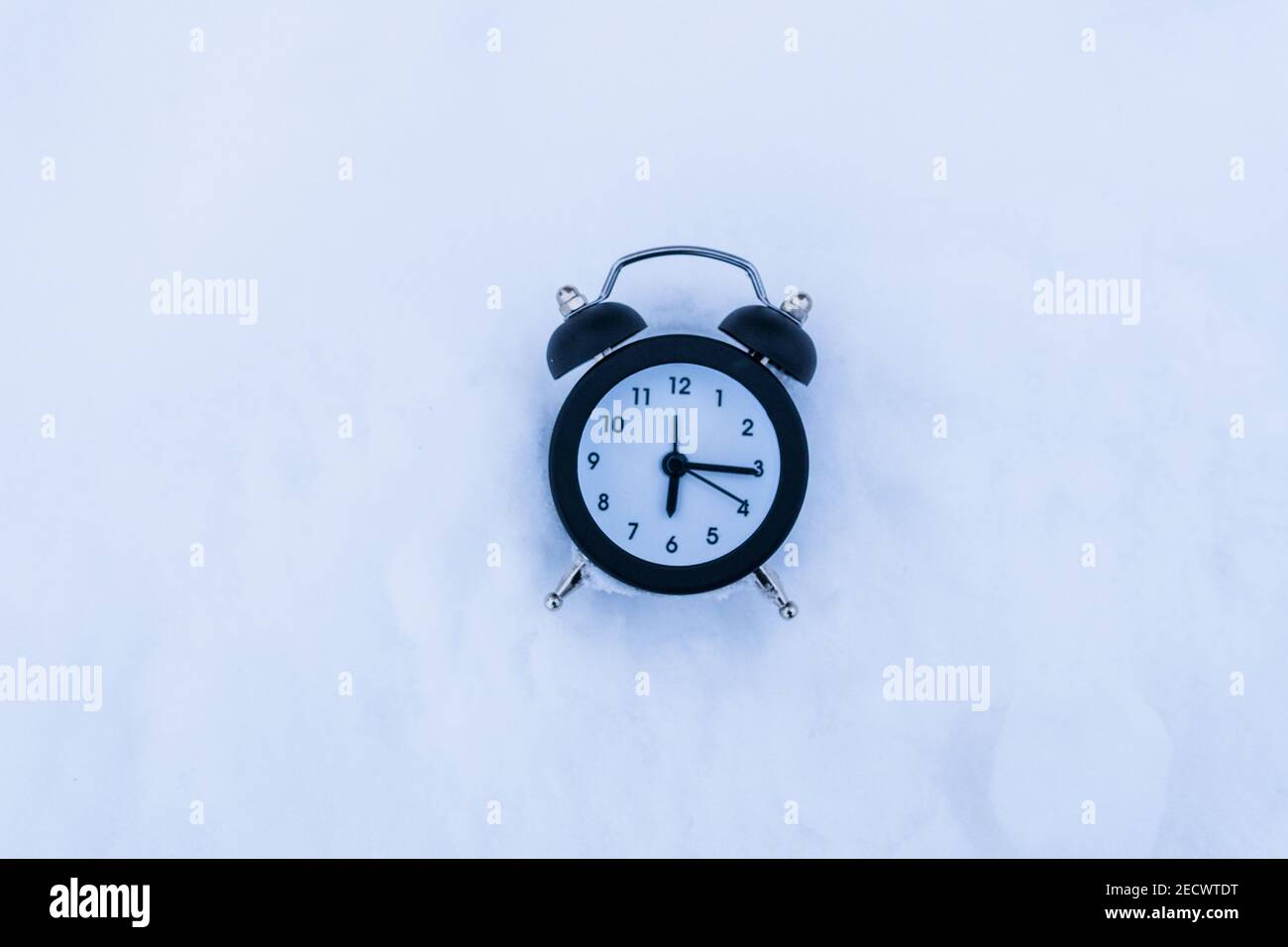 alarm clock in snowy weather on a winter background. Return to winter ...