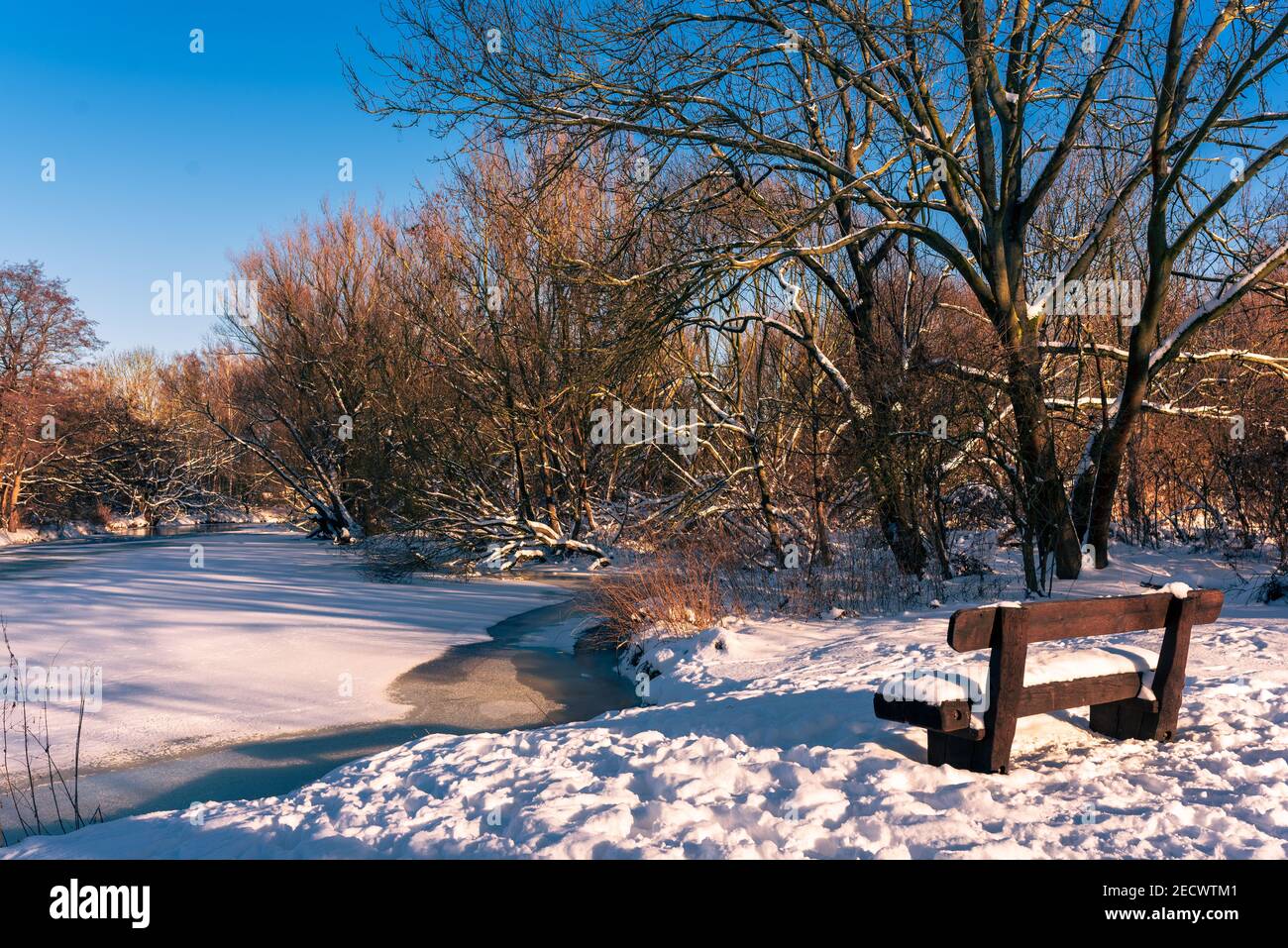 a park bench in the snow by the frozen river Stock Photo