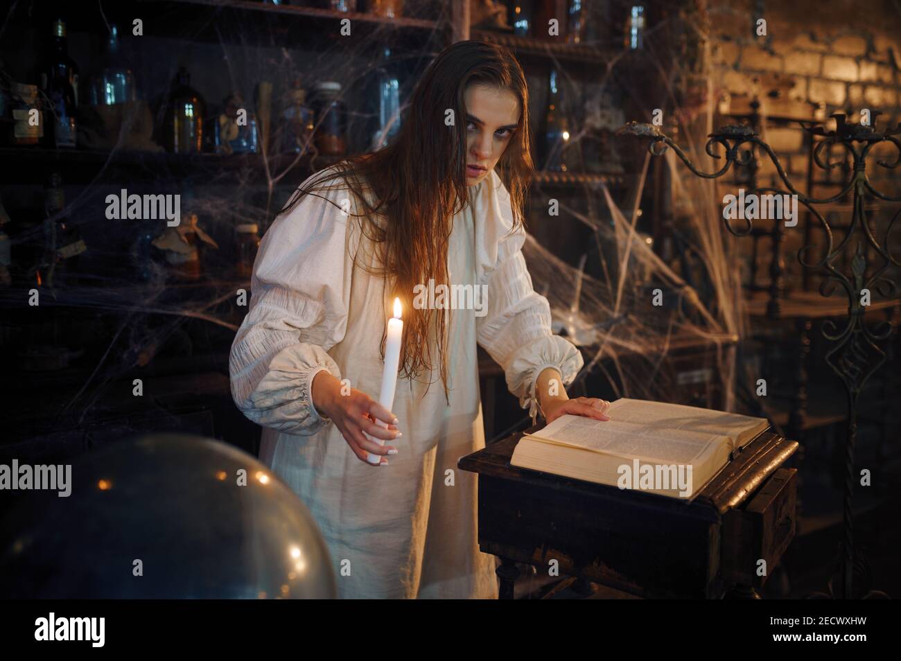 Demonic woman with candle reads book of spells Stock Photo