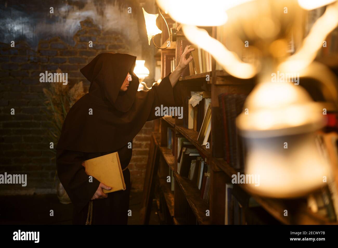 Exorcist in black hood choosing book of spells Stock Photo