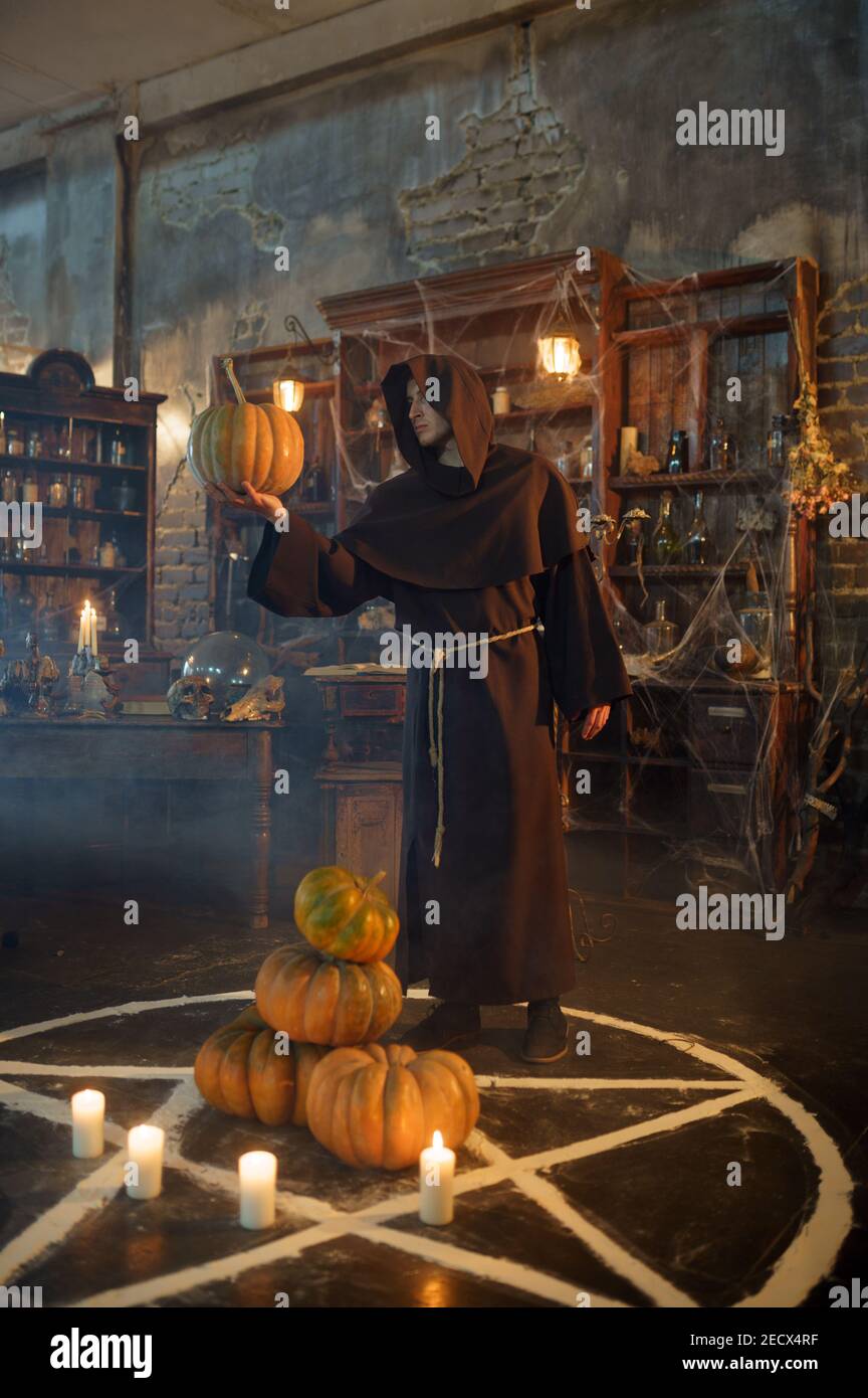 Exorcist in hood holds pumpkin near magic circle Stock Photo