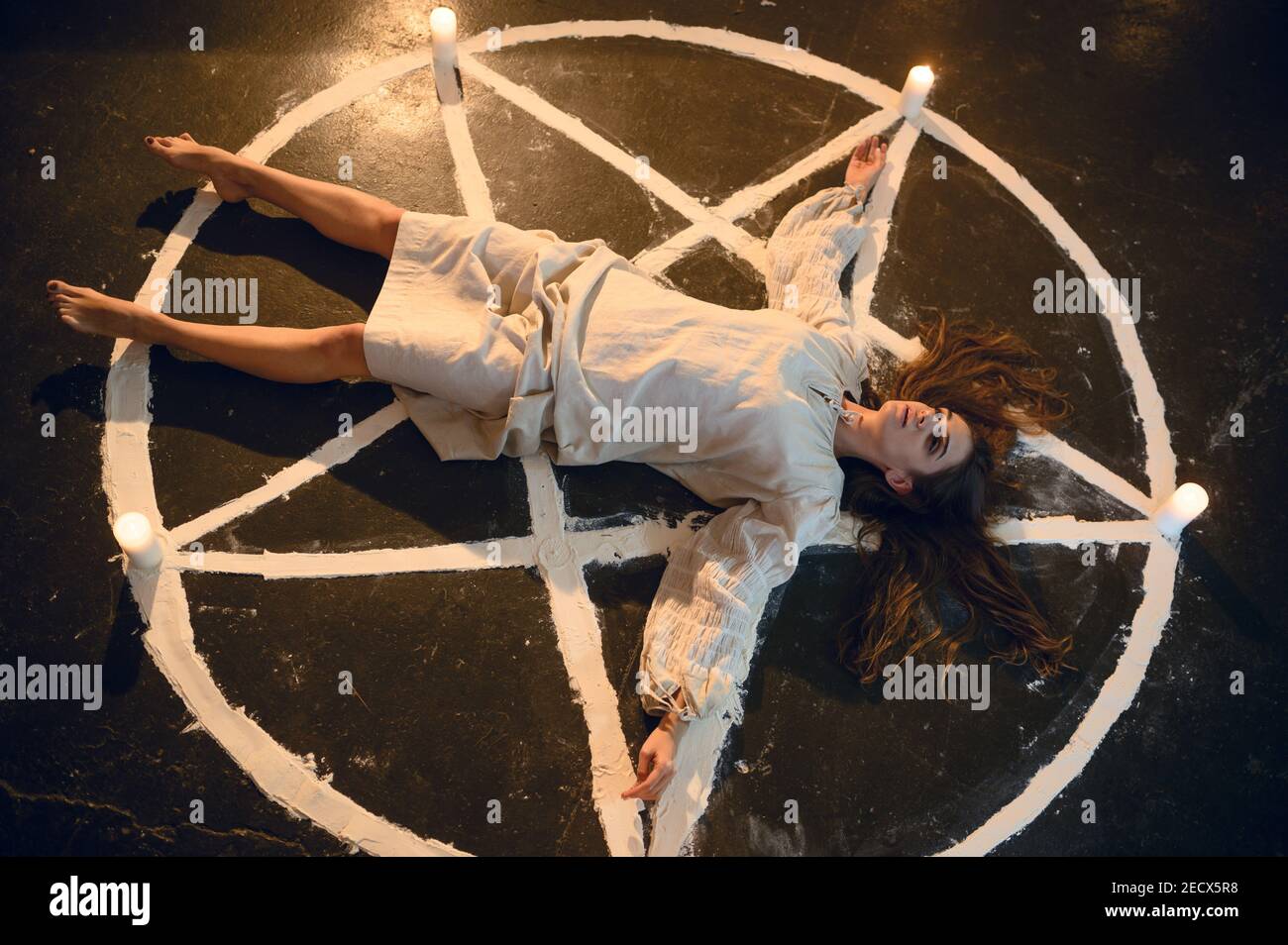 Demonic woman lying in magic circle with candles Stock Photo