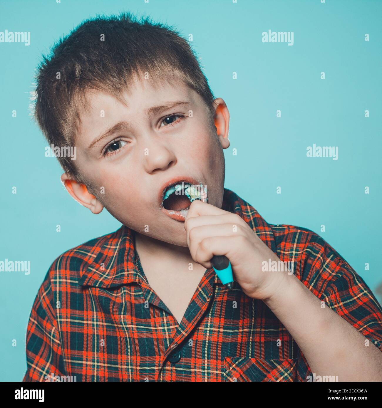 Daily oral hygiene procedure, the boy follows the rules of cleanliness and oral hygiene. A boy brushing his teeth in disgust and grimacing at toothpas Stock Photo