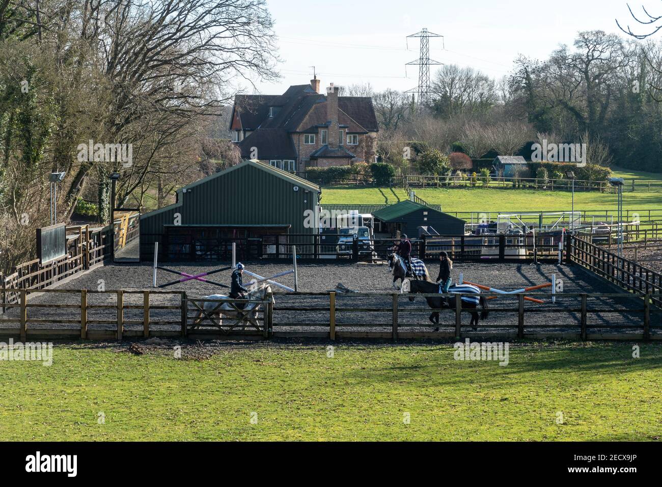 Outdoor horse riding arena at riding school with three riders on horses, Hampshire, England, UK Stock Photo