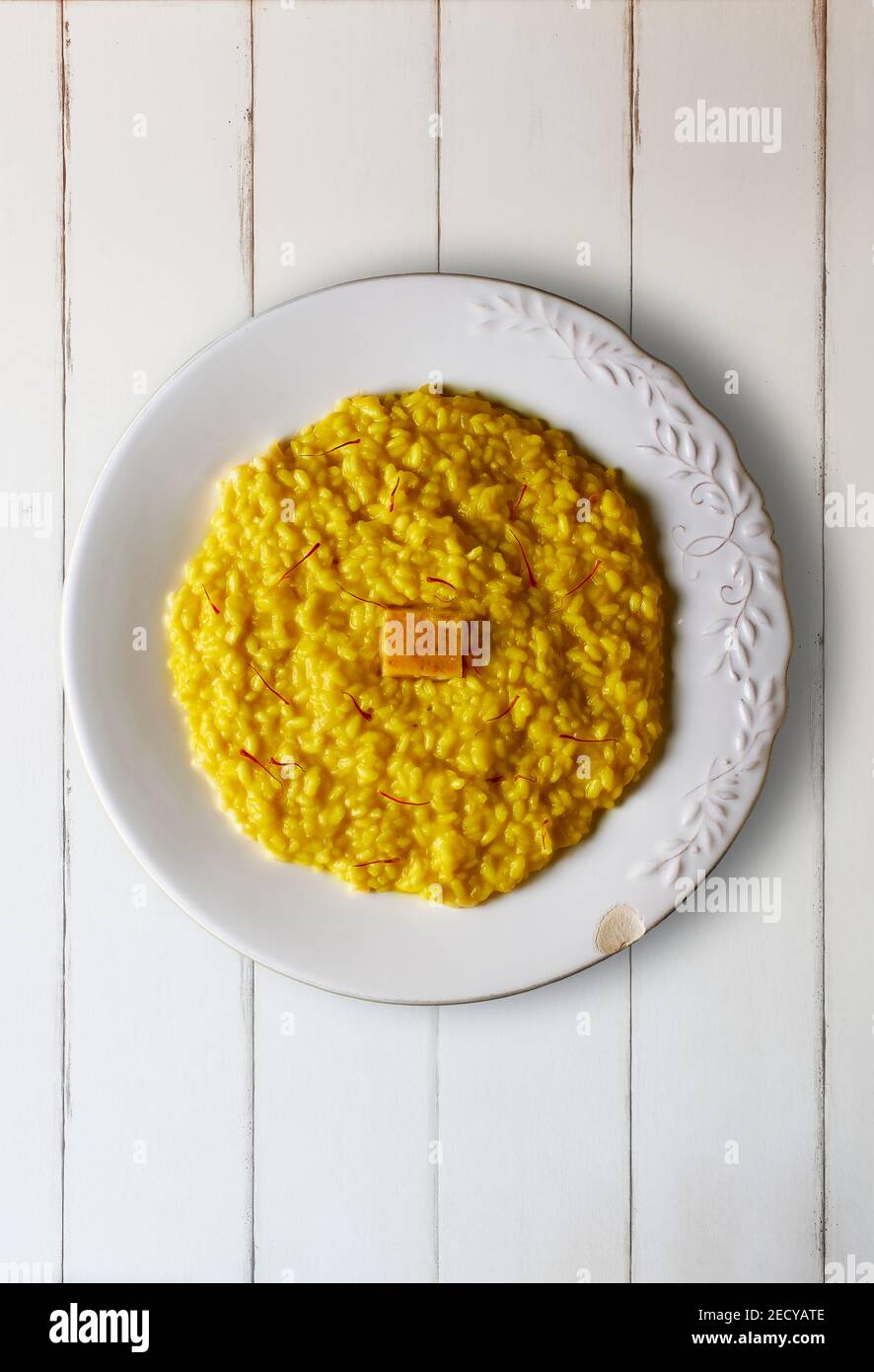 Risotto alla Milanese dressed with saffron threads and a Parmigiano Reggiano cheese rind on a white wooden table. Italian cuisine. Stock Photo