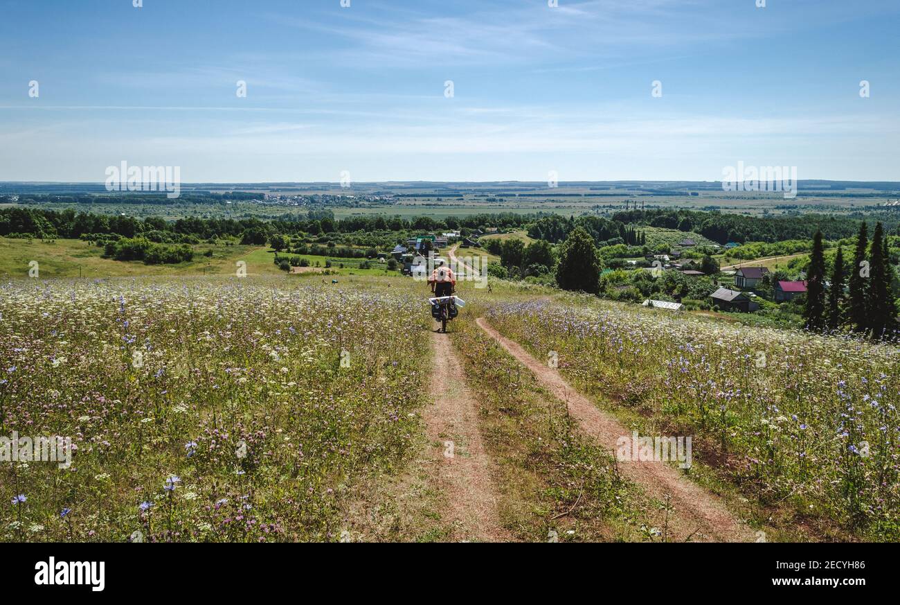Traveling cyclist on rural dirt field, cycle route, summer landscape Stock Photo
