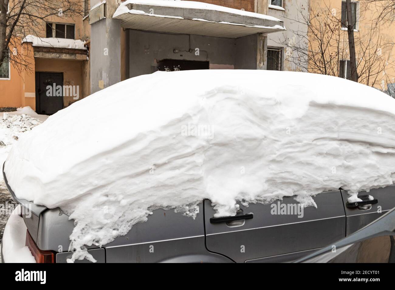 old abandoned broken car parked by the road under a large layer of snow ...