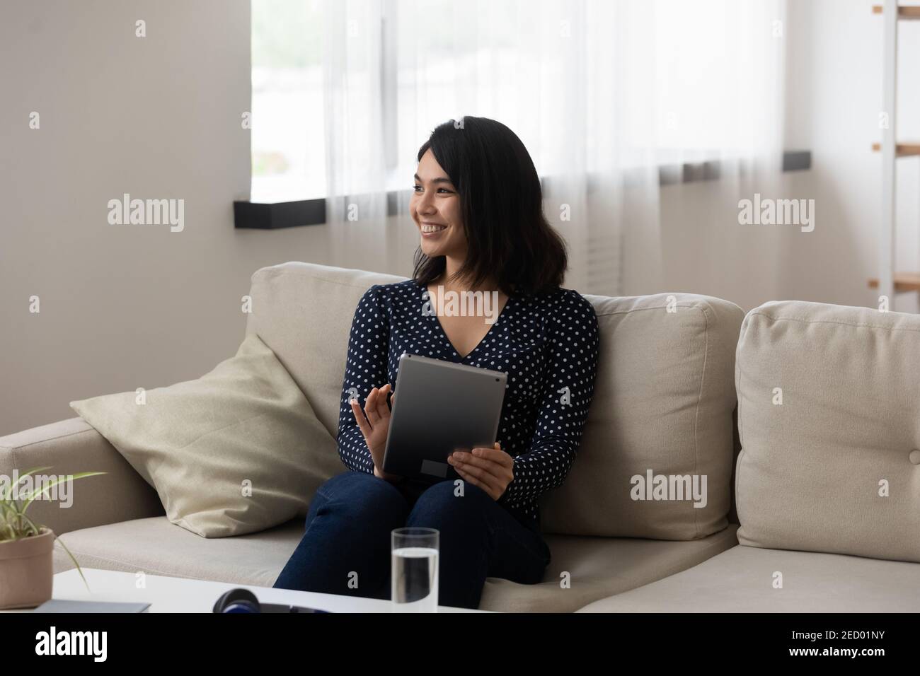 Smiling young asian female sit on couch working on tablet Stock Photo ...