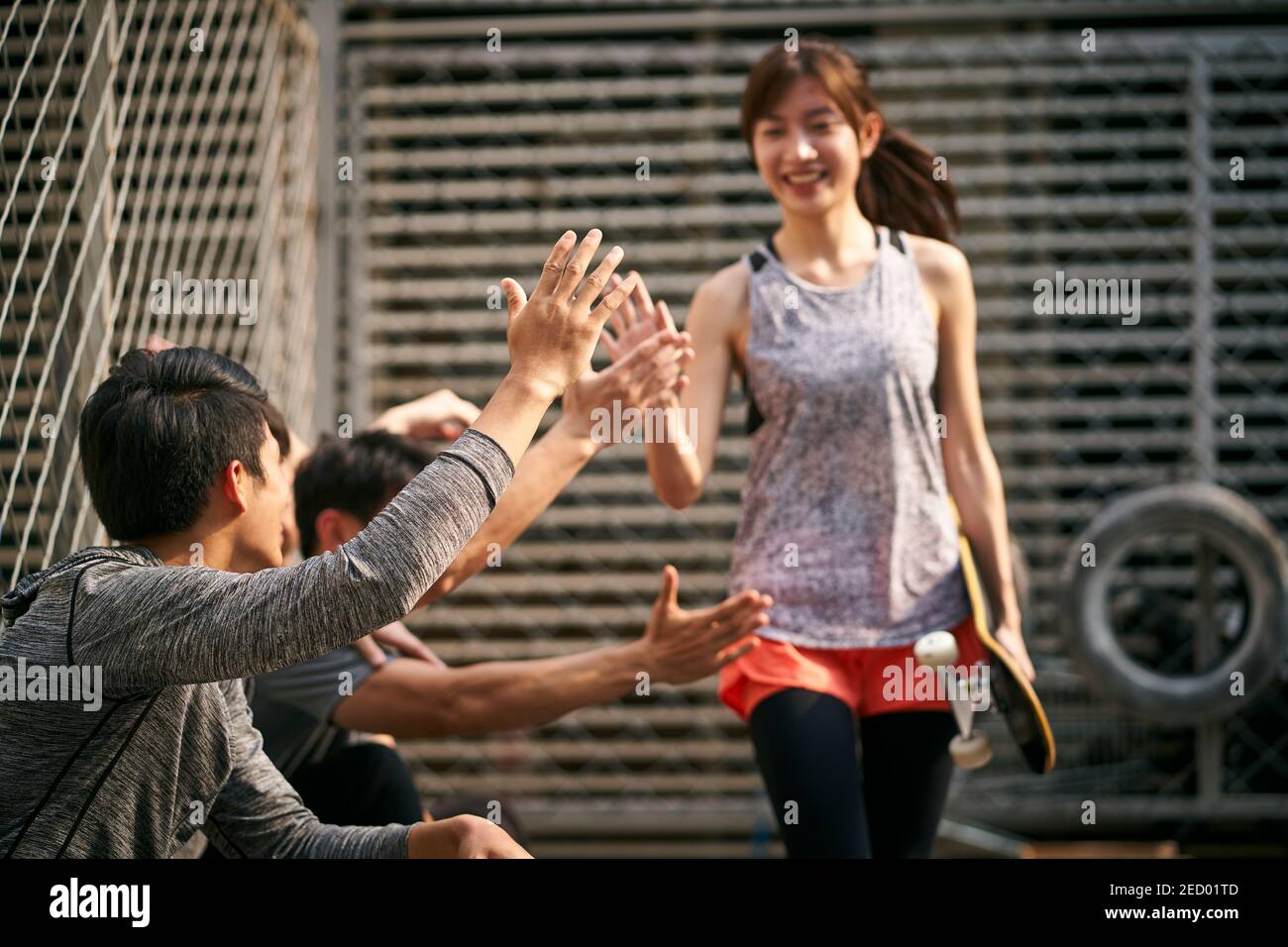 young asian adult woman skateboarder giving a group of young men hi-five, focus on hand Stock Photo
