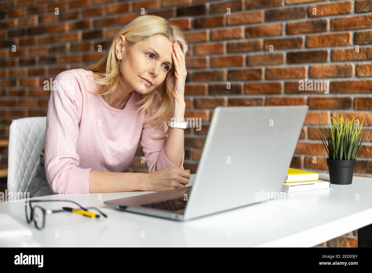Discouraged middle-aged woman sitting at the laptop,does not know what to do,at office,looking at laptop screen,worried and tired, an entrepreneur Stock Photo