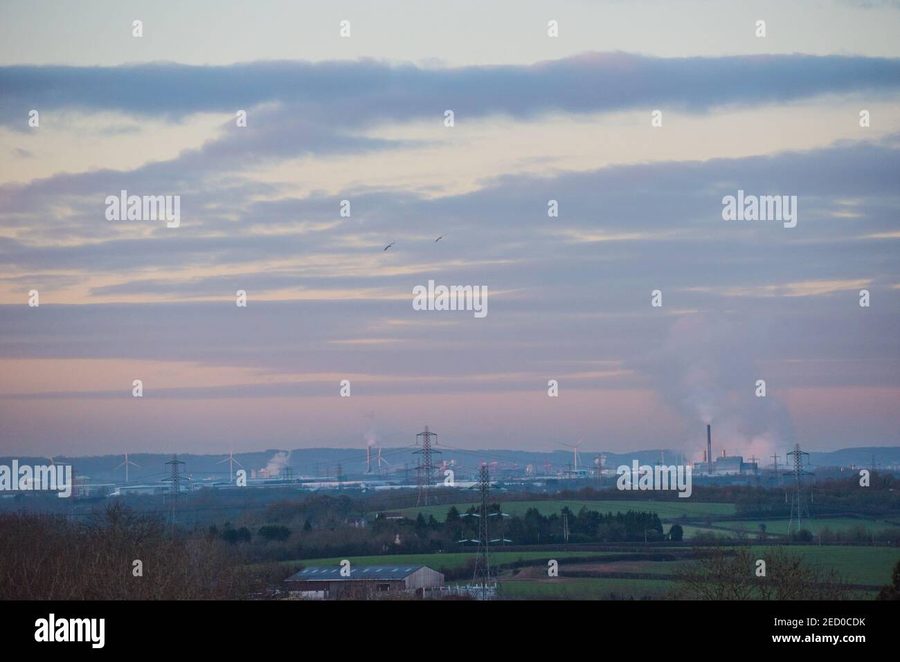 View across countryside to industrial Avonmouth and the Seabank Power Station pumping out plumes of steam, over wind turbines and electricity pylons Stock Photo