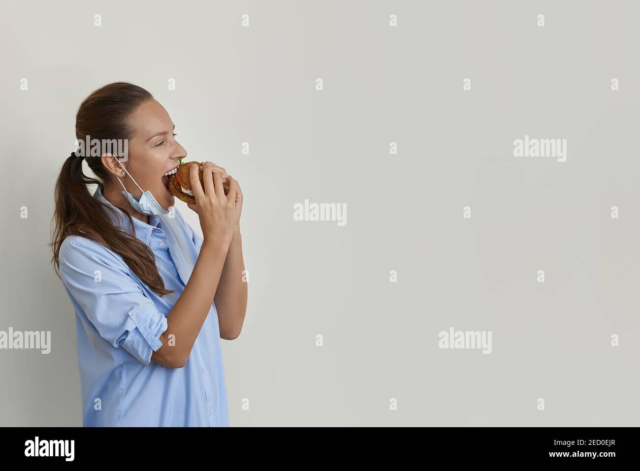 Pretty woman in mask eating a vegan burger side view Stock Photo