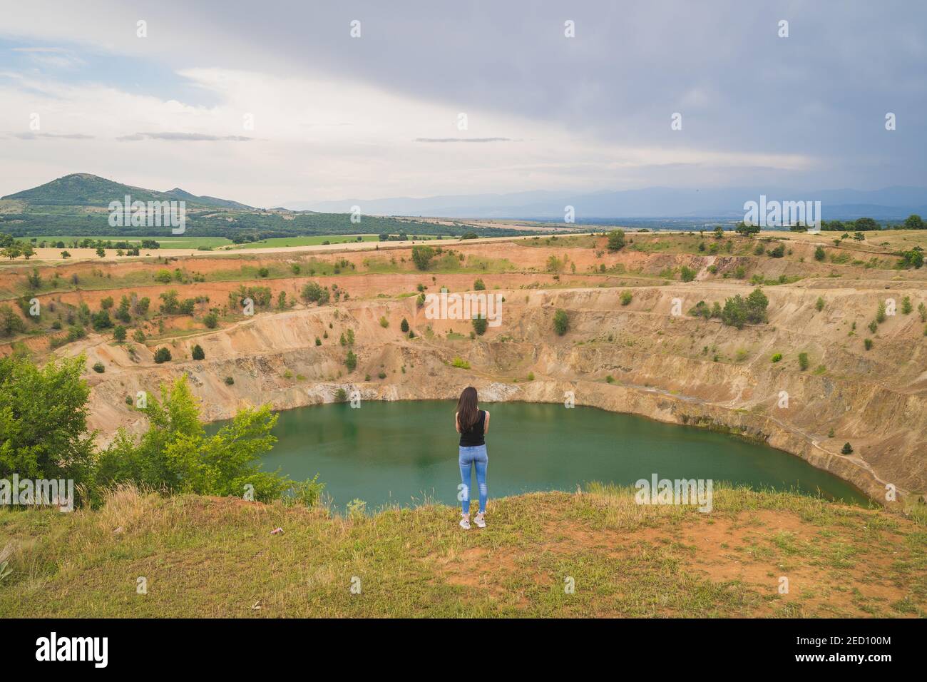 Panoramic view of young fit woman looking at big abandoned copper mine pit full of water in Bulgaria Stock Photo