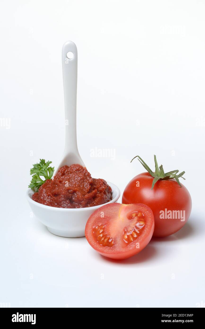 Tomato paste with spoon in bowl, whole and half tomato on white
