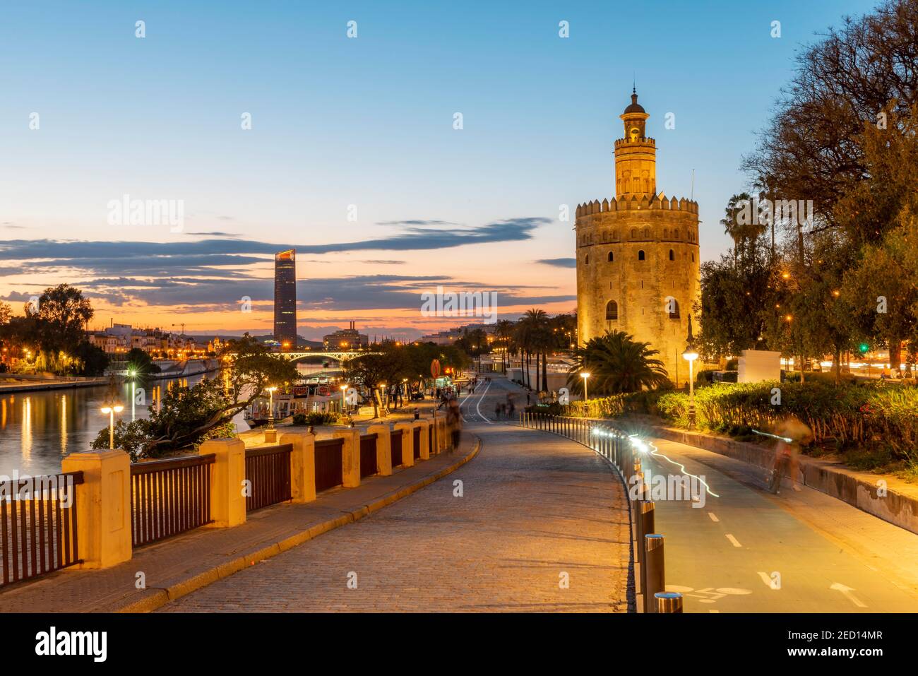 Boardwalk at the river Rio Guadalquivir with illuminated Torre del Oro, in the back Torre Sevilla, sunset, blue hour, Sevilla, Andalusia, Spain Stock Photo