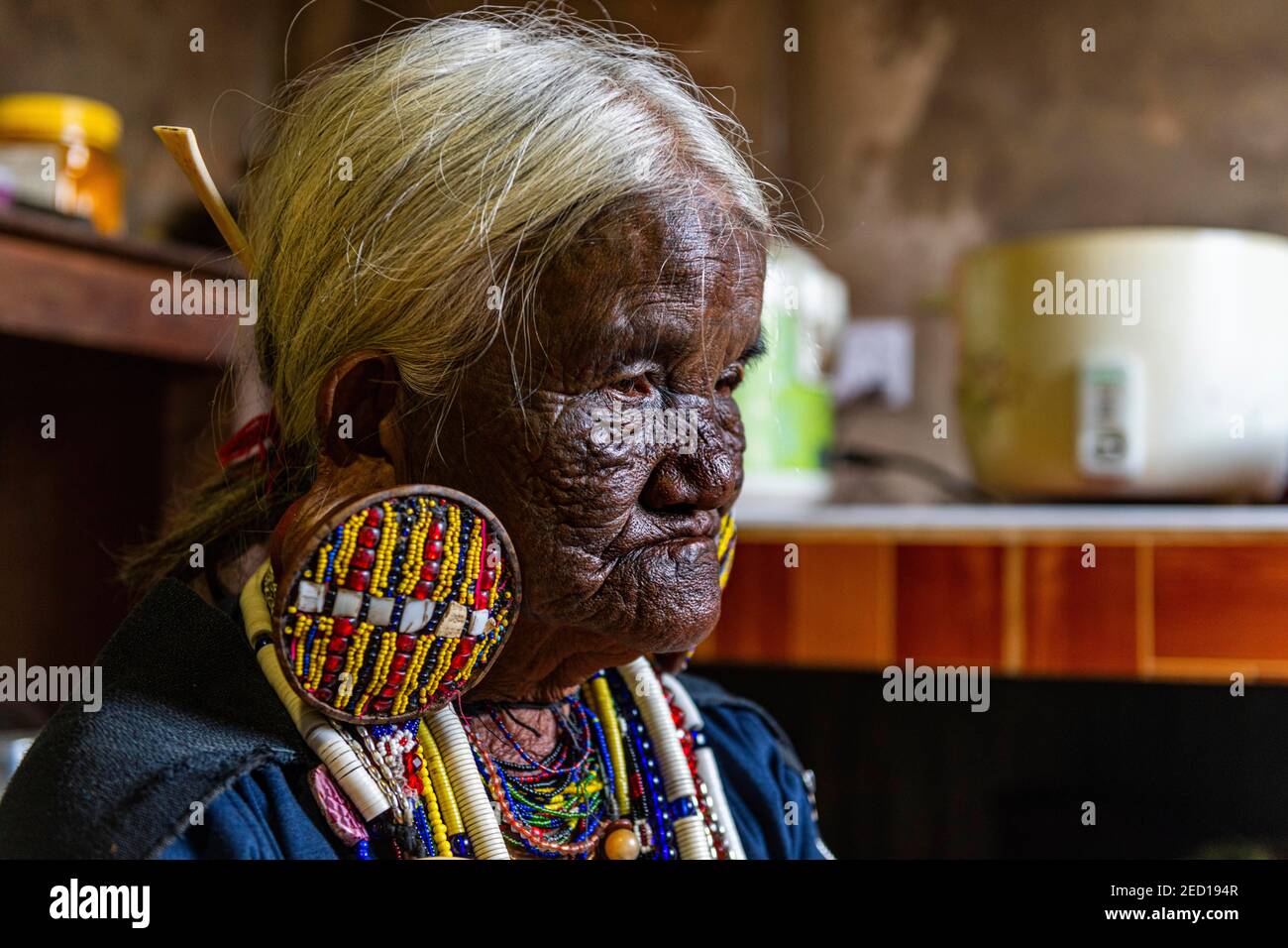 Chin Kaang hill-tribe woman with traditional facial tattoo and elaborate tribal earrings playing a flute with her nose, Mindat, Chin state, Myanmar Stock Photo