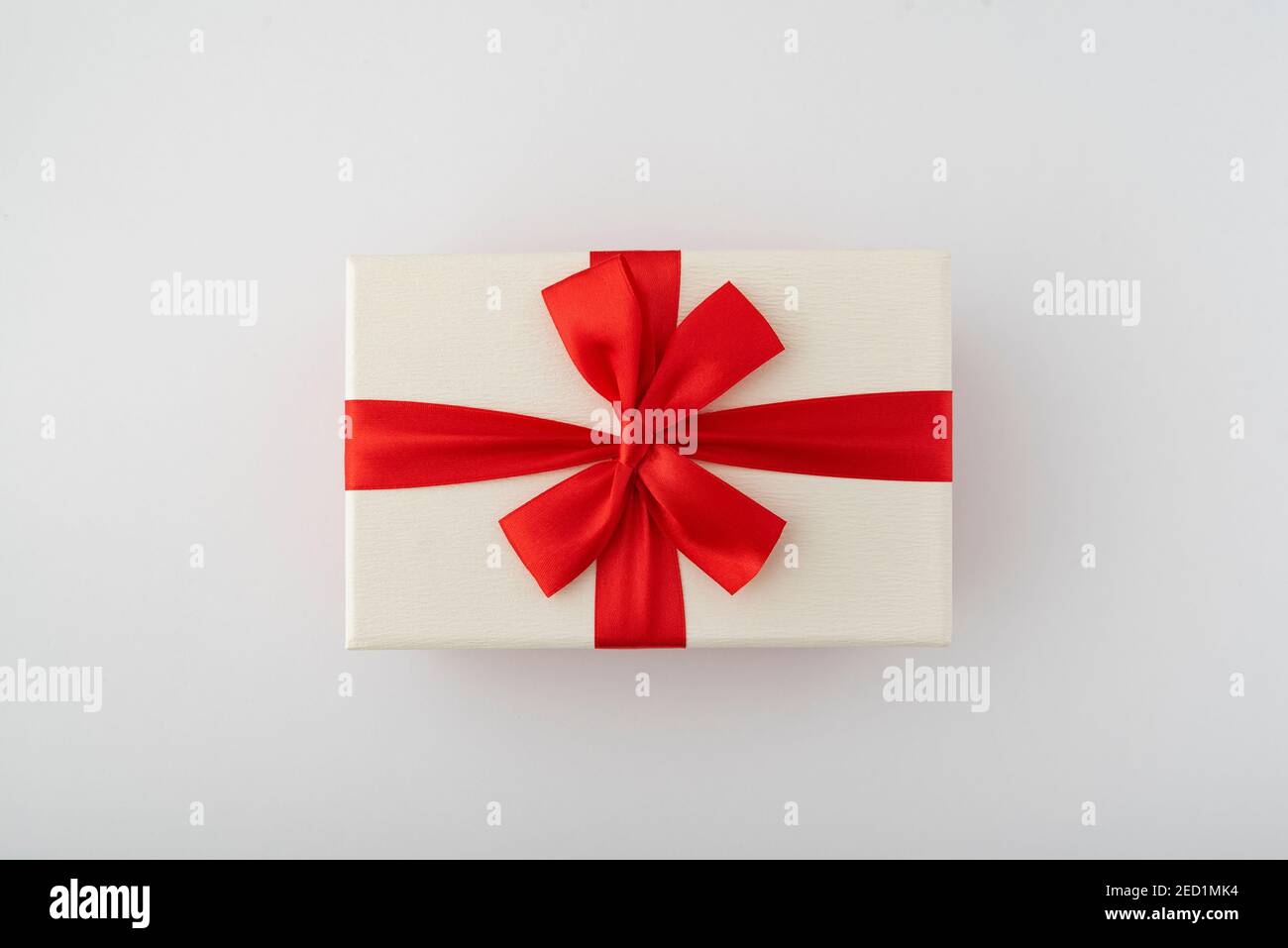 White gift box with red ribbon and bow on white background. Top view ...