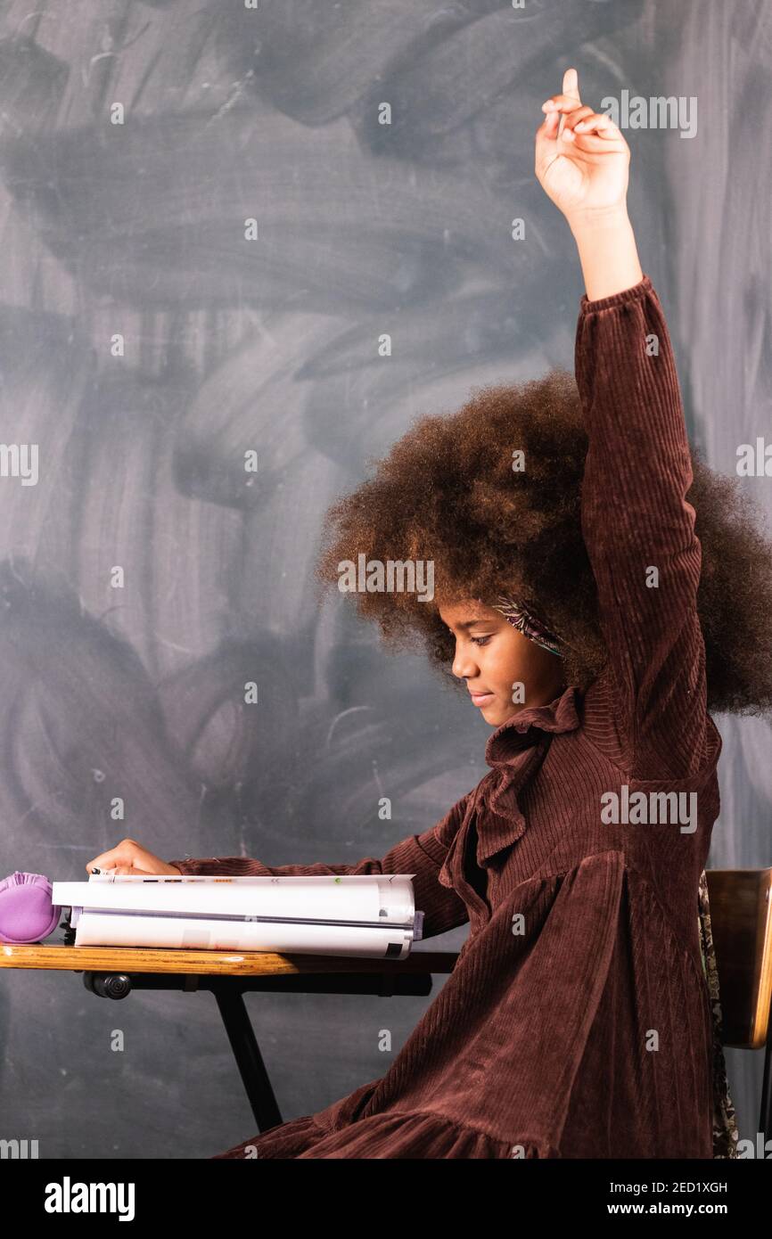 Side view of African American schoolgirl sitting with raised hand in ...