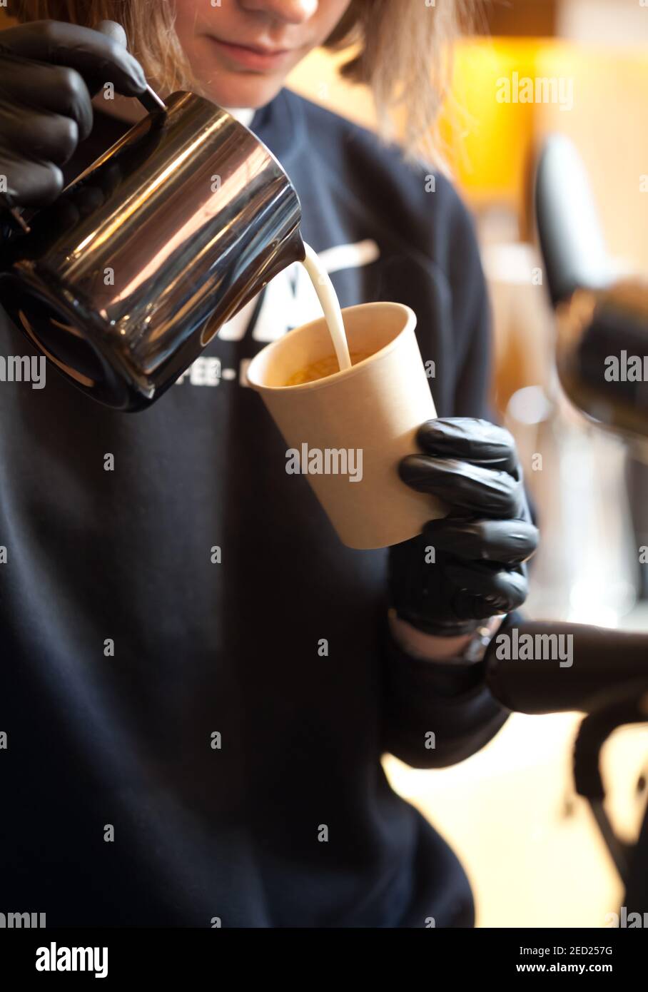 barista pouring milk from pitcher into paper cup, take away coffee, closeup Stock Photo