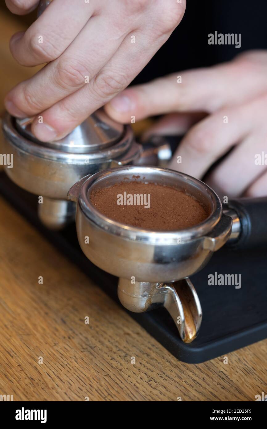 barista hands temping coffee grind in espresso holder during coffee preparation, closeup Stock Photo