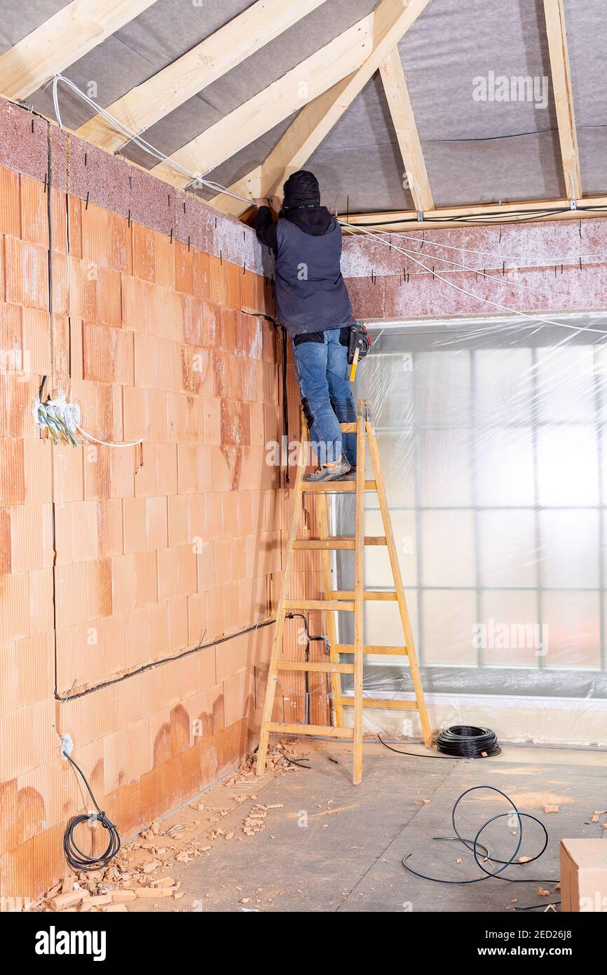 Electrician standing on ladder installing cables in the channel