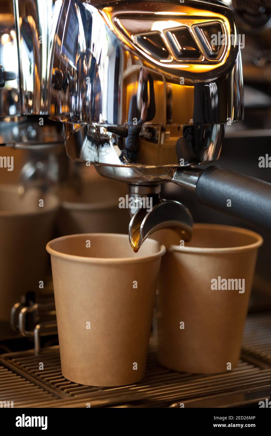 coffee pouring from professional espresso machine into take away paper cup, closeup Stock Photo