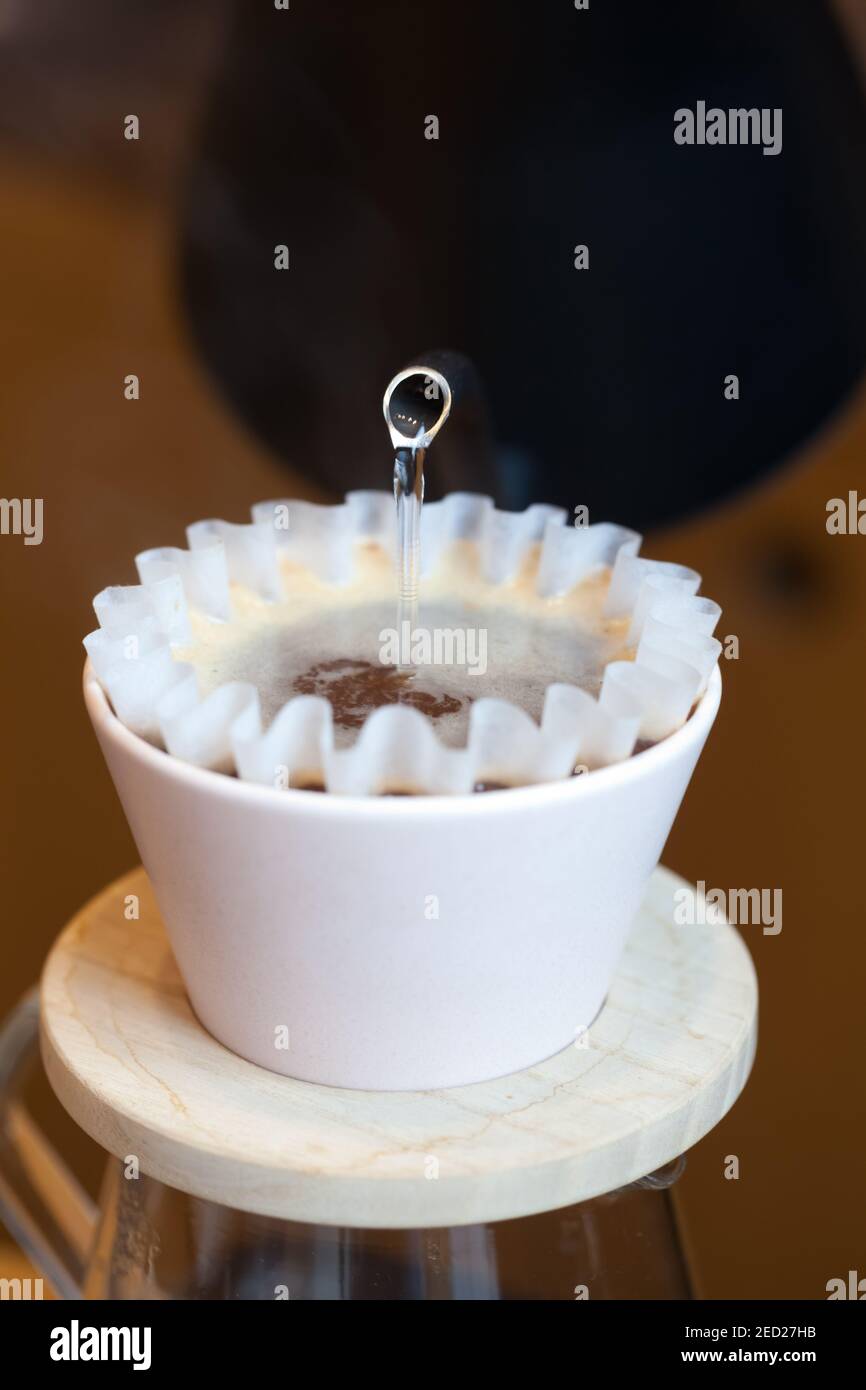 front view of kettle pouring hot water into kalita pour over paper filter, coffee brewing Stock Photo