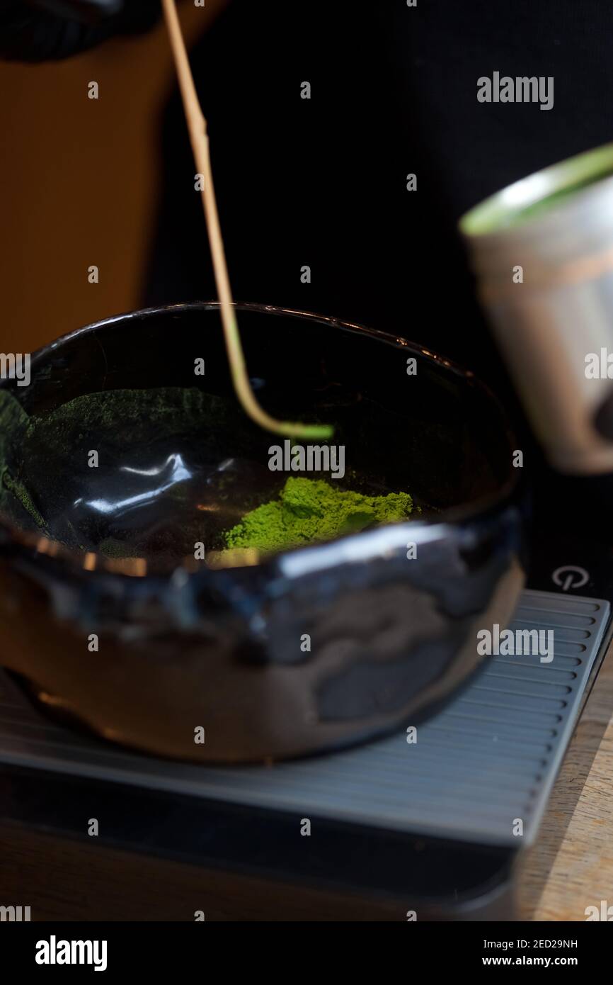 weighing green powder matcha tea in dark ceramic bowl on scales, macro closeup, no people Stock Photo