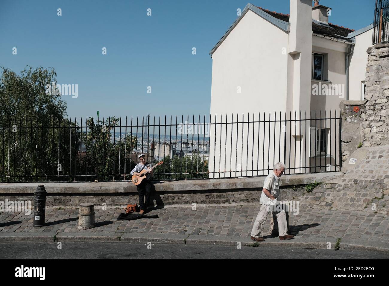 MONTMARTRE, PARIS - 29TH JUNE 2019: An elderly man walking past a musician busking on Rue Saint-Éleuthère in Montmartre. Stock Photo