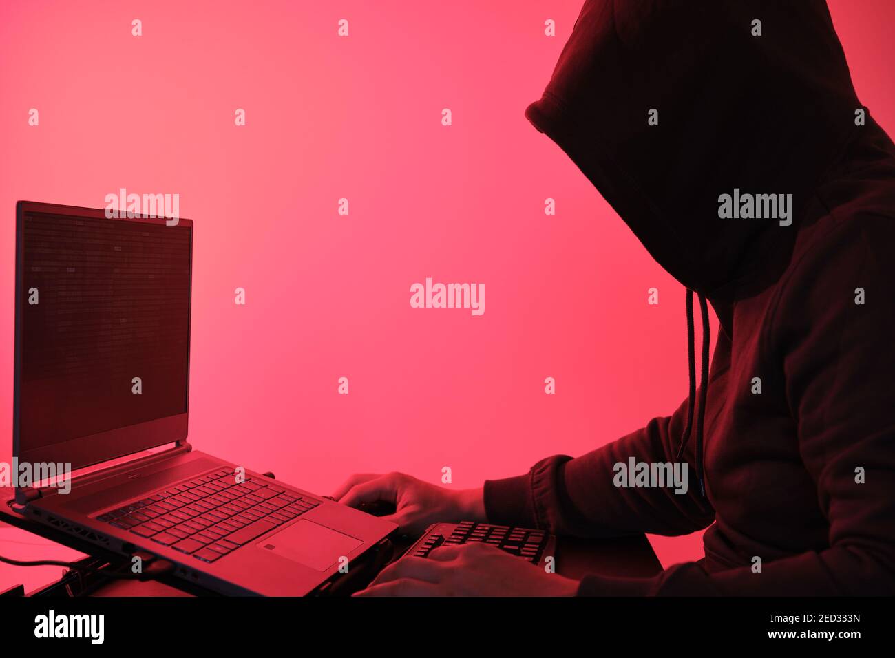 Hooded hacker in front of a computer for organizing massive data breach attack around the world. Cyber criminal concept. Stock Photo
