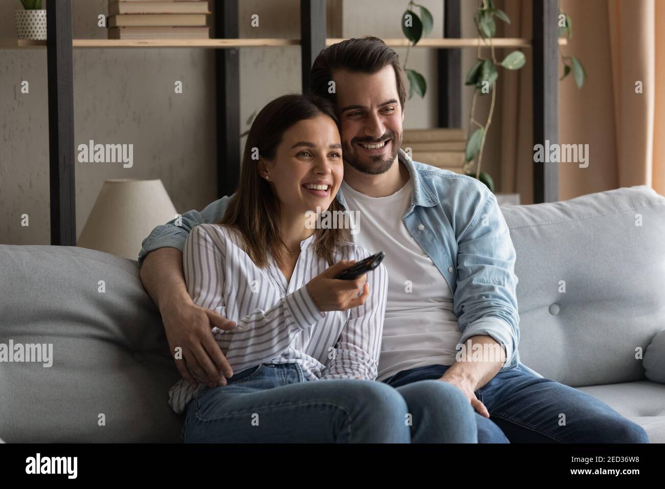 Bonding millennial couple hugging on sofa watching movie on tv Stock Photo