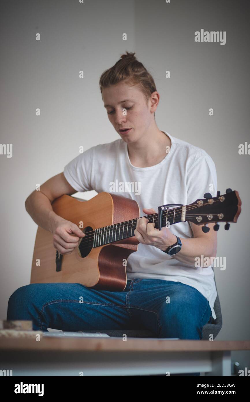 young blond boy is trying to learn a new skill and that is playing a musical instrument - an acoustic guitar. The product of singing and moving your h Stock Photo