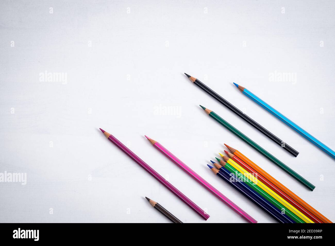 Many colored crayons are placed in an inclined position like arrows on a white background, ample space available for text. Stock Photo