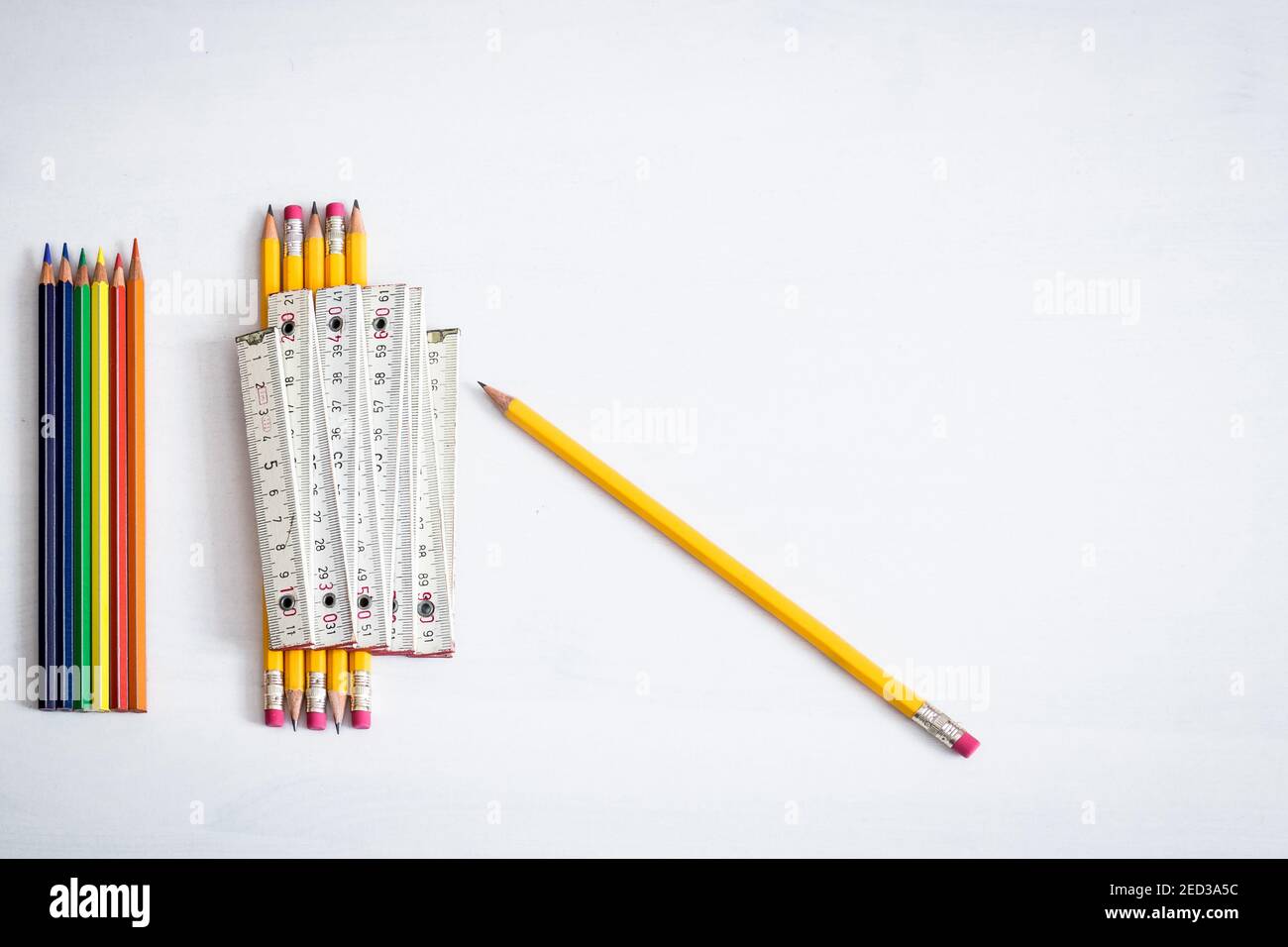 A group of coloured crayons and pencils resting on a white background with one meter indicating the safe distance to keep in enclosed places. Stock Photo