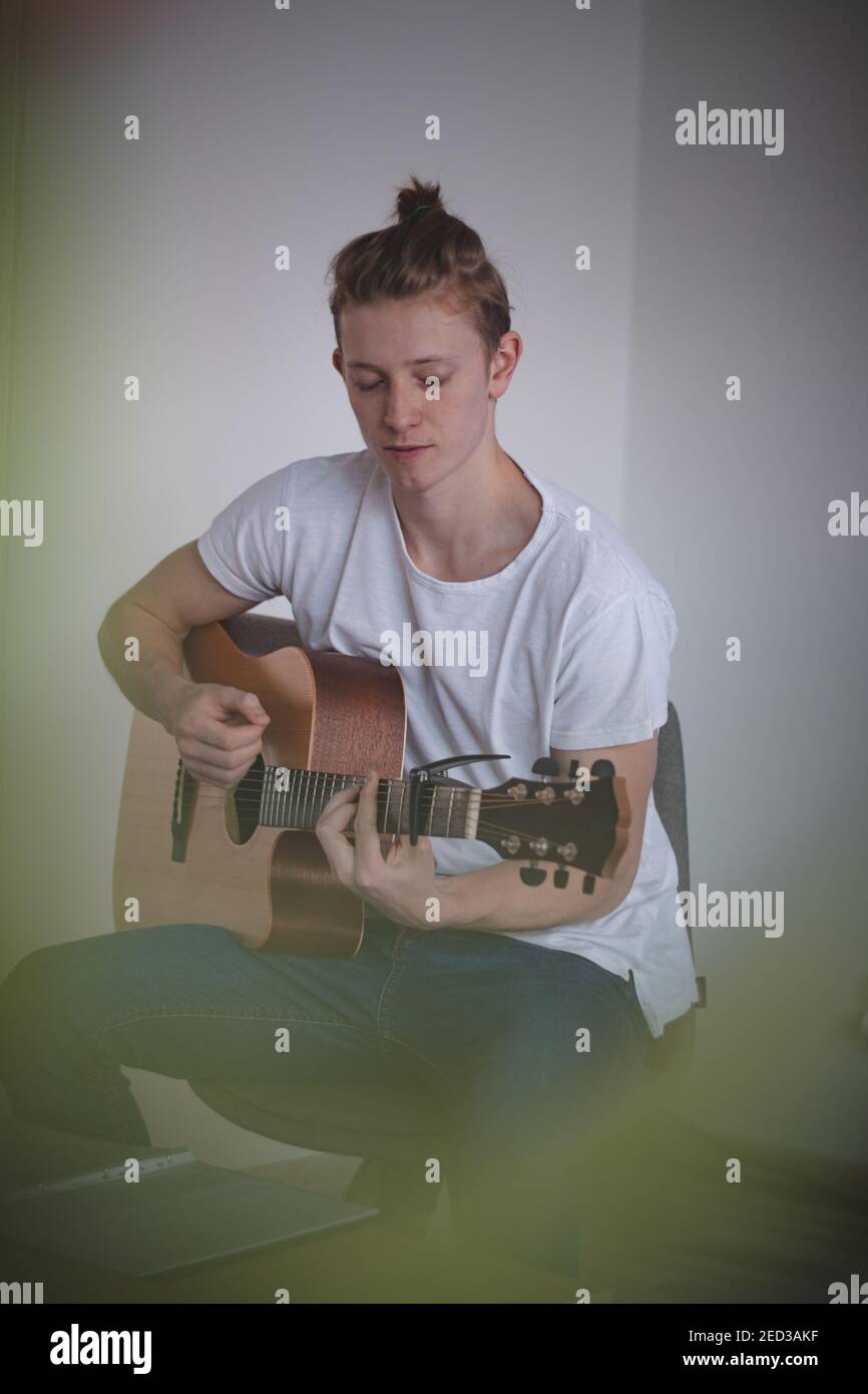 Casual-looking blond boy with freckles spends his free time playing his memorial guitar and singing a love song. Music class. Practicing chords during Stock Photo