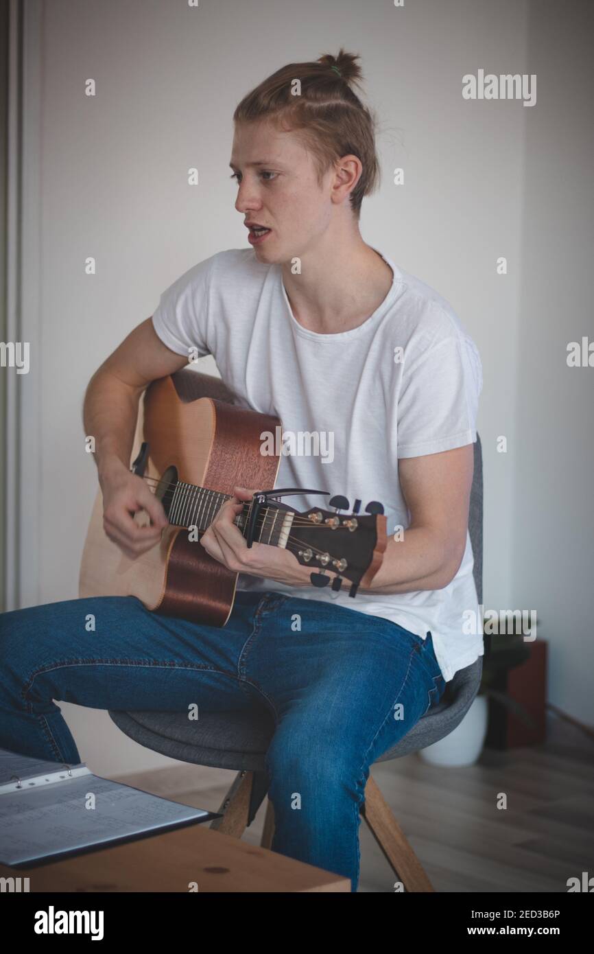 singing blond man with freckles sits in the middle of a lighted room. Practicing chords and songs in your spare time after work. The singer relives hi Stock Photo