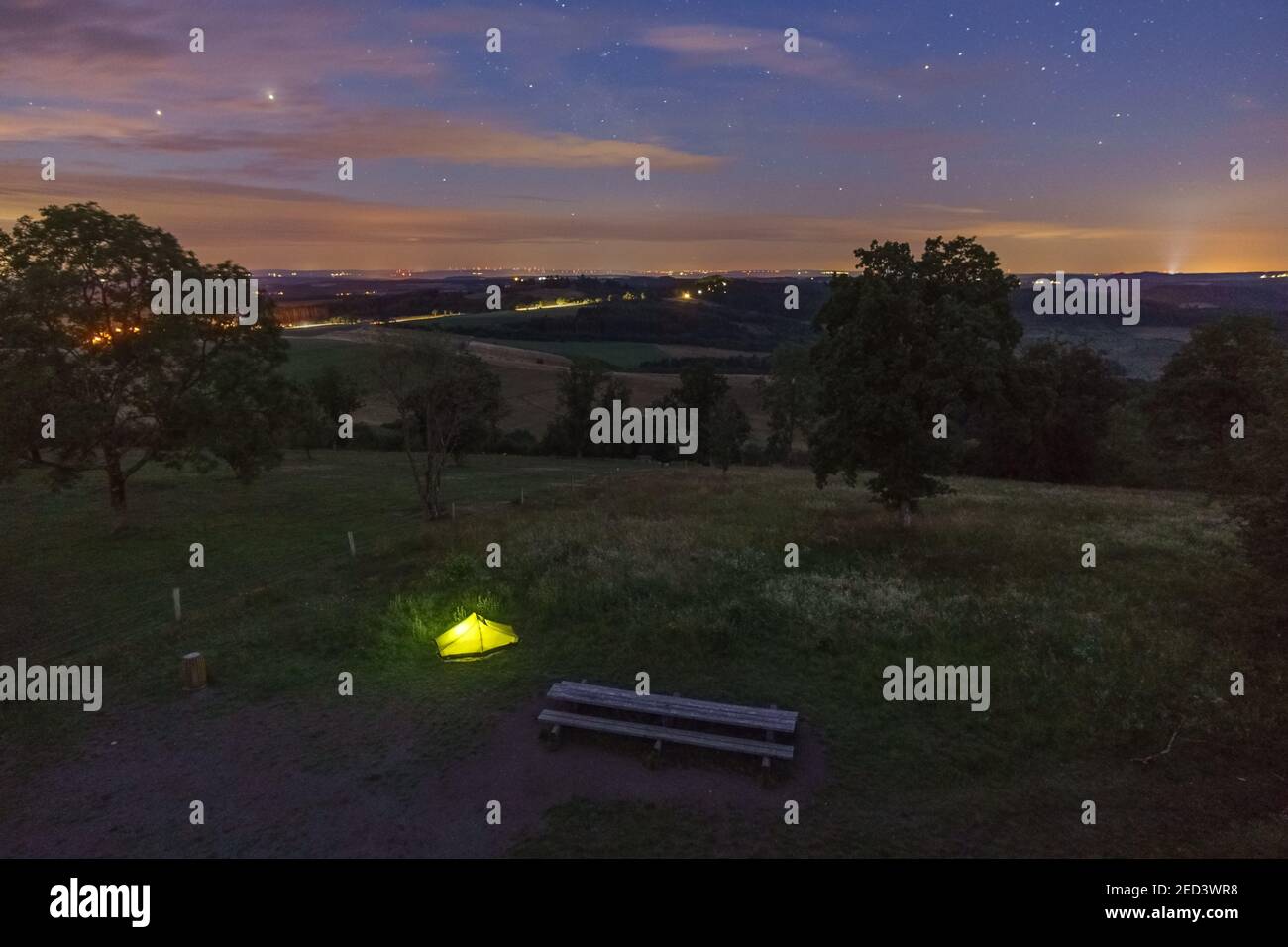 Illuminated green camping tent in resting area from high angle view at night in rural german eifel landscape, Germany Stock Photo