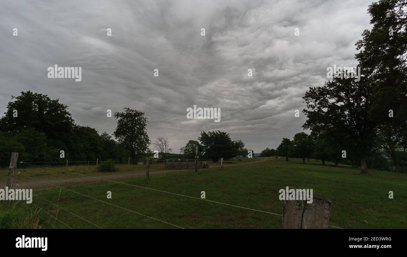 dark structured clouds over hiking path on pasture in the morning, Germany Stock Photo