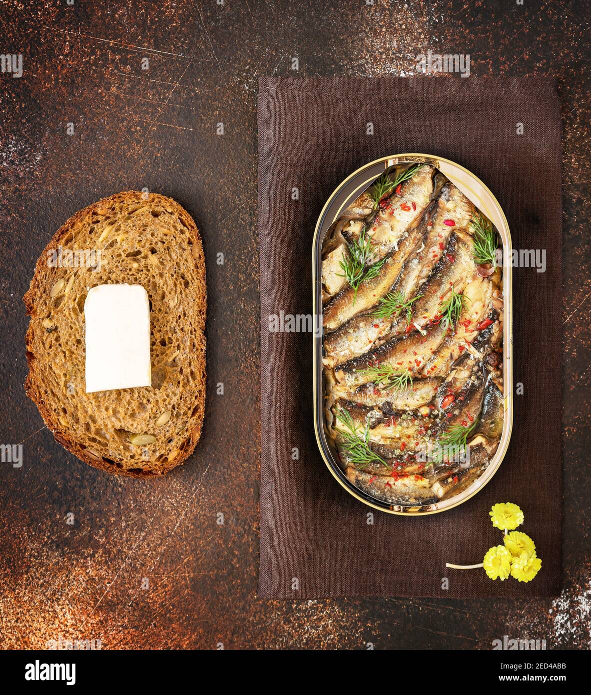 Open tin of Baltic sprats in oil with spices, a slace of bread with butter on an old brown background. Fish appetizer with beer. Traditional baltic, s Stock Photo