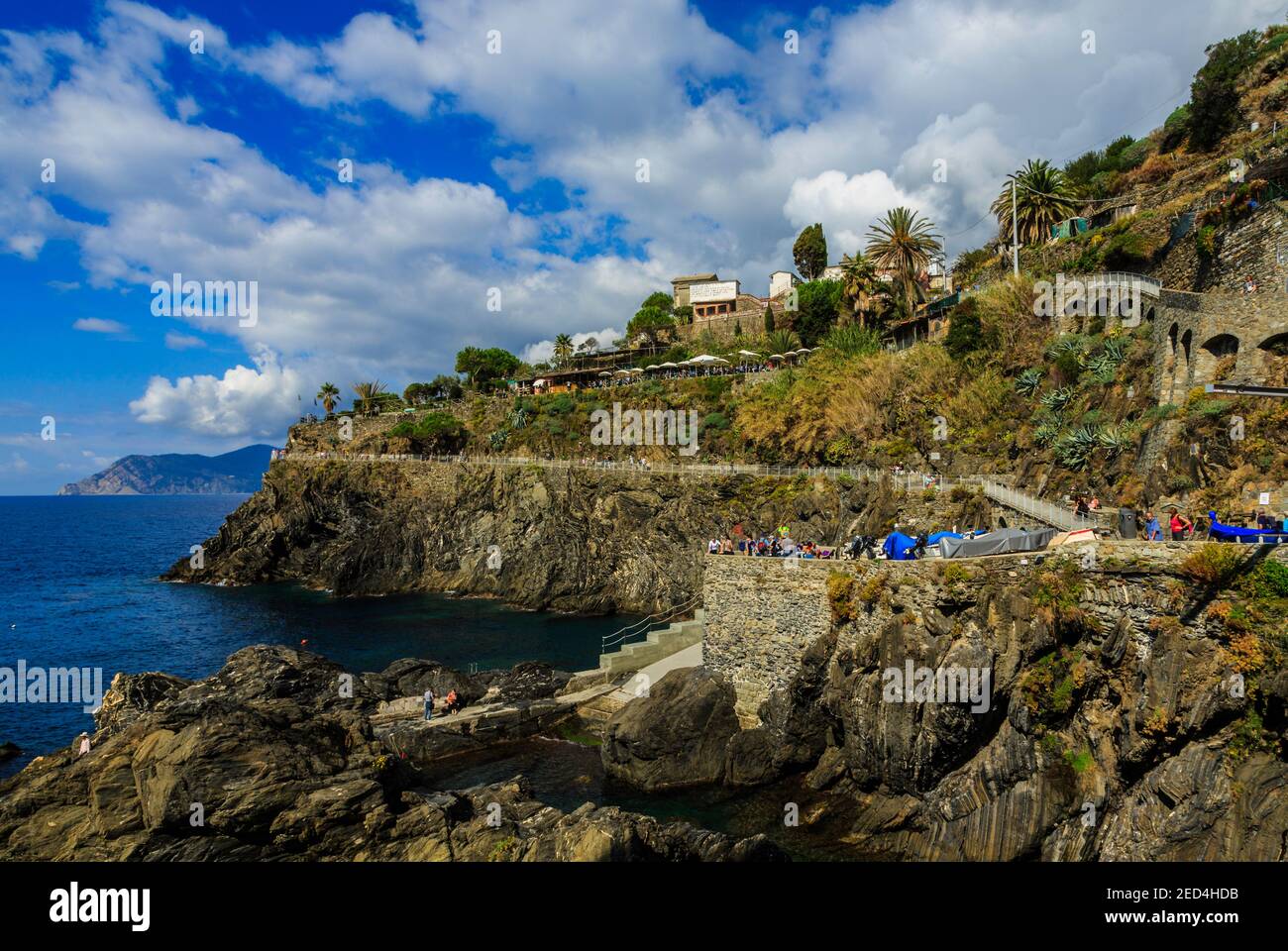 Beautiful seaside day on the rocky coastline and waterfront of Manarola, Cinque Terre, Italy, with a long look down the distant mountains and coast. Stock Photo