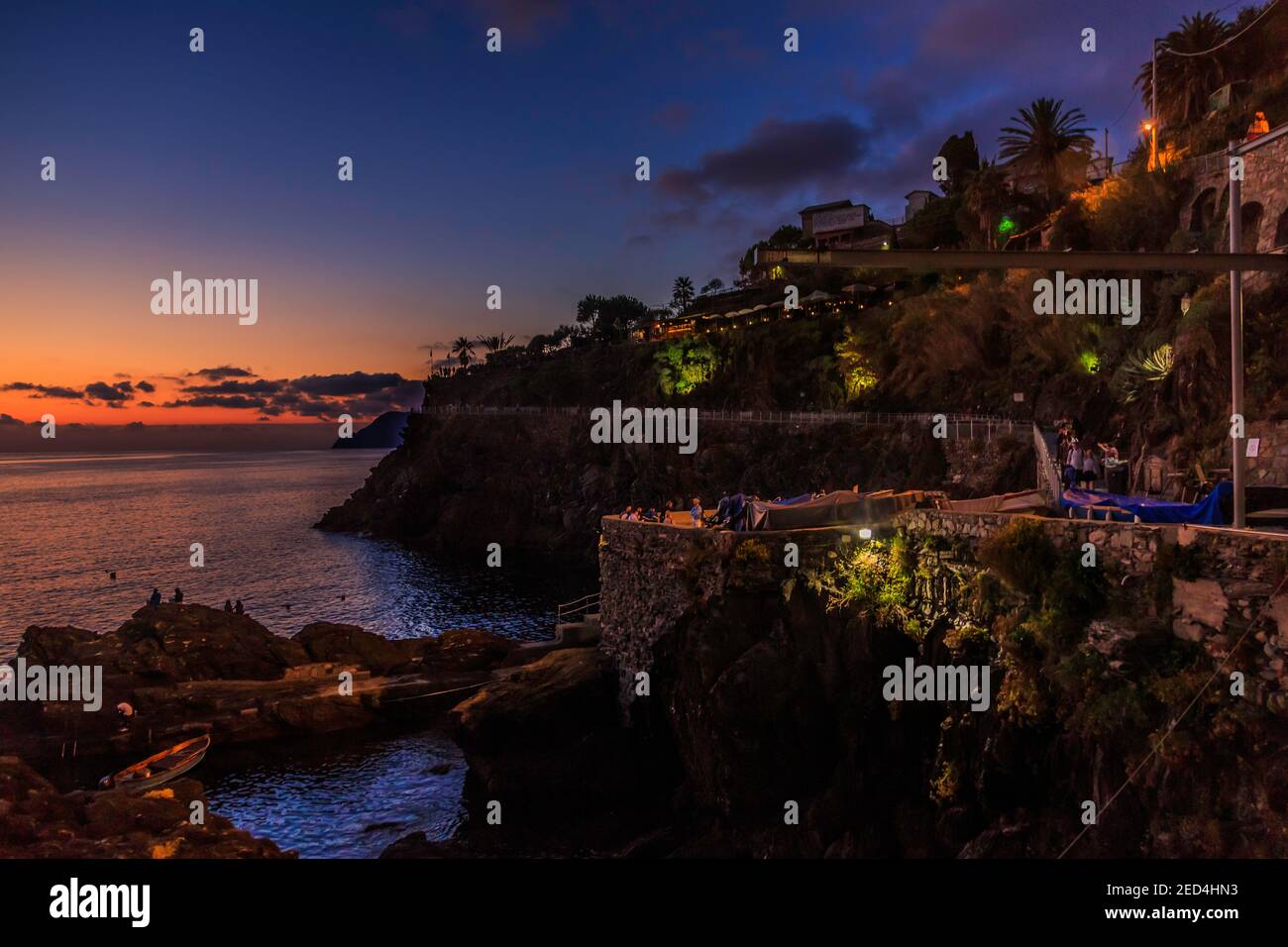 A beautiful sunset afterglow lights the horizon as viewed from the steep, rocky village waterfront in Italy's Cinque Terre. Stock Photo