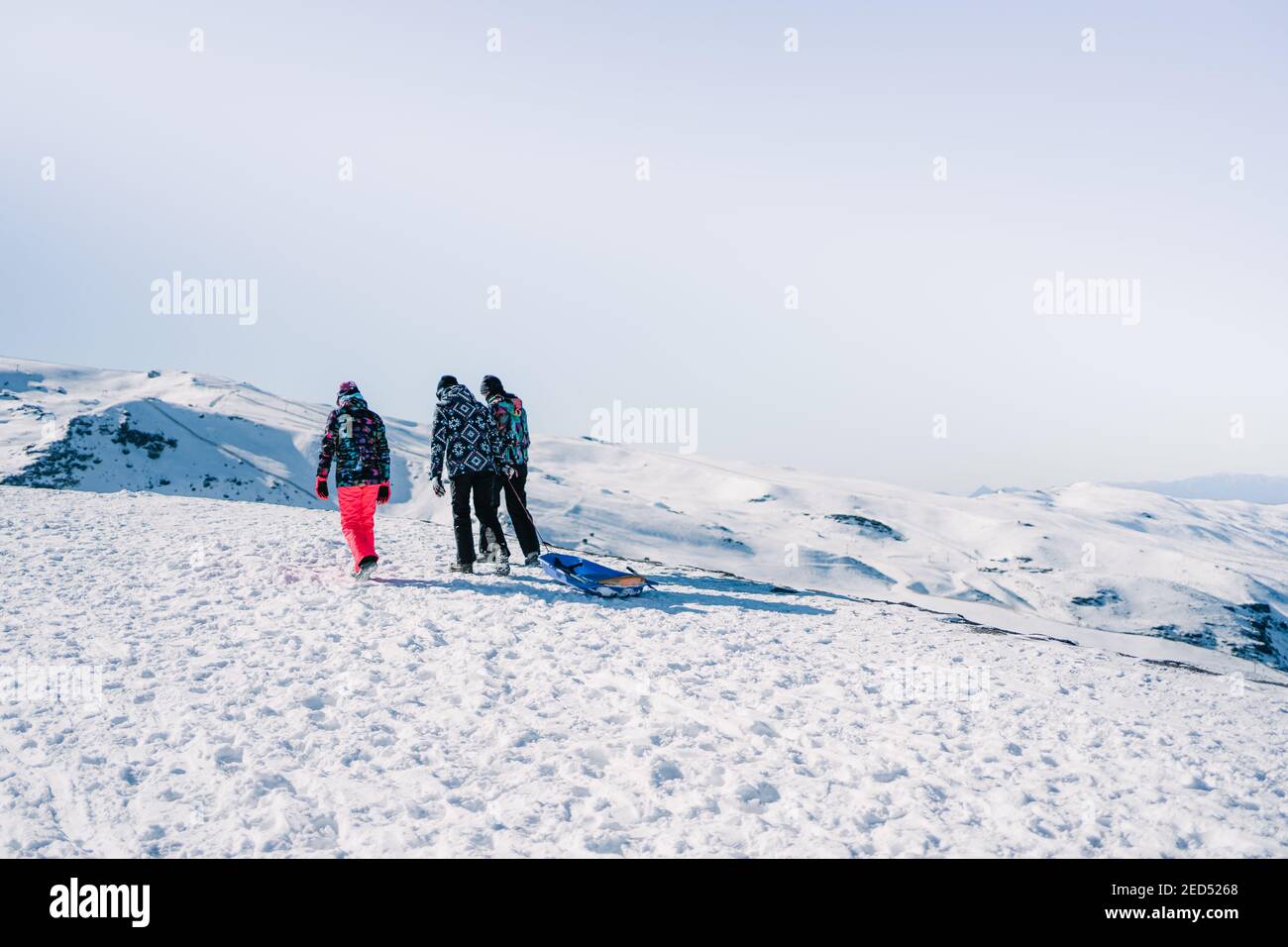 Three unrecognizable people walking with a sled in the snow wearing ...