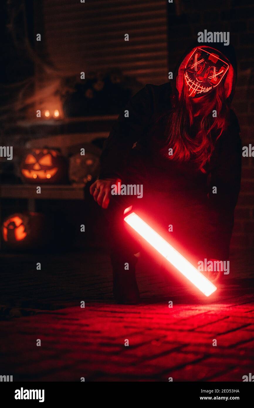 A closeup view of a girl with a red glowing dead mask with a lightsaber ...